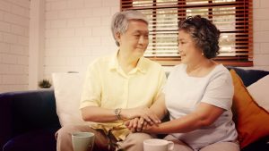 Couple de personnes âgées asiatique tenant leurs mains tout en prenant ensemble dans le salon,