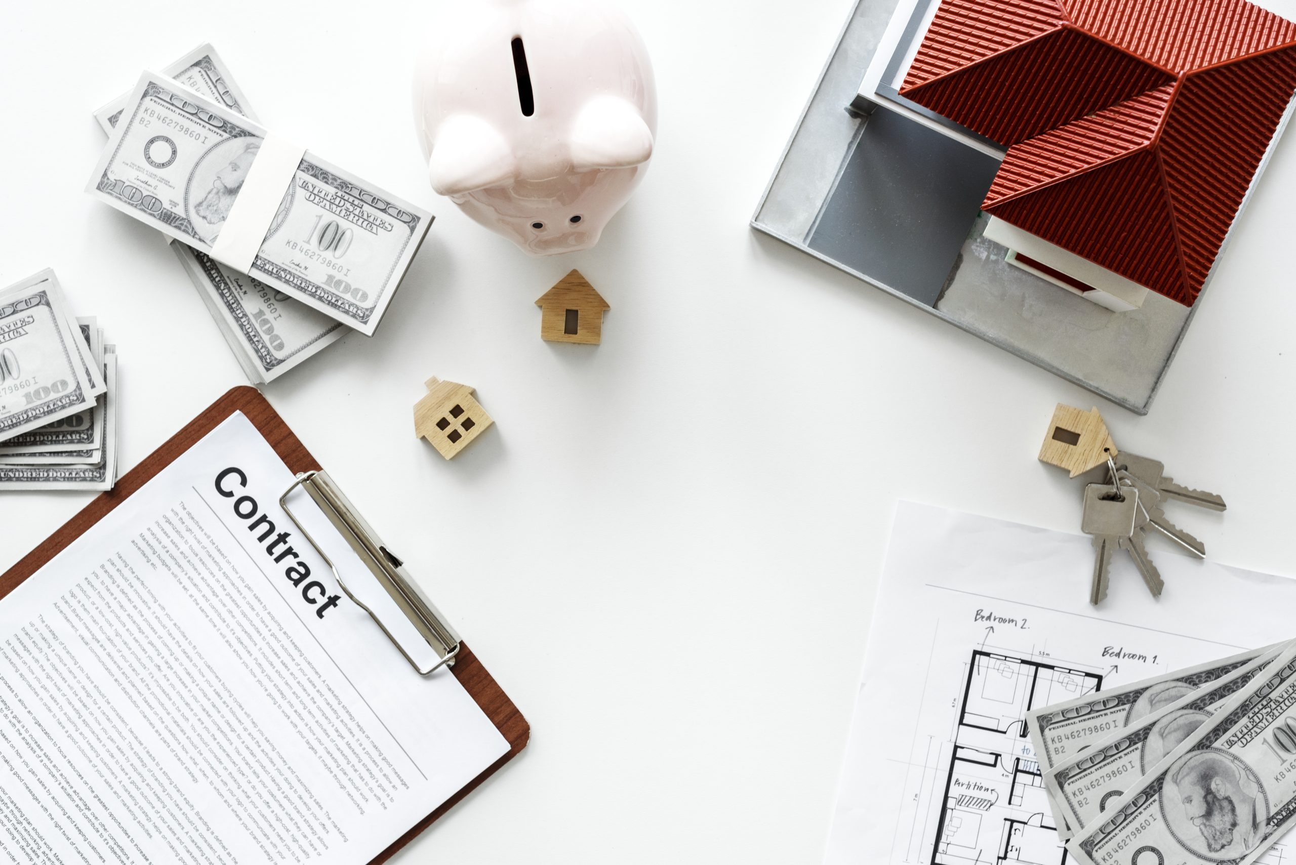 Mise à plat du concept de défiscalisation immobilière avec un modèle de maison, un contrat, des billets de dollars et une tirelire sur fond blanc
