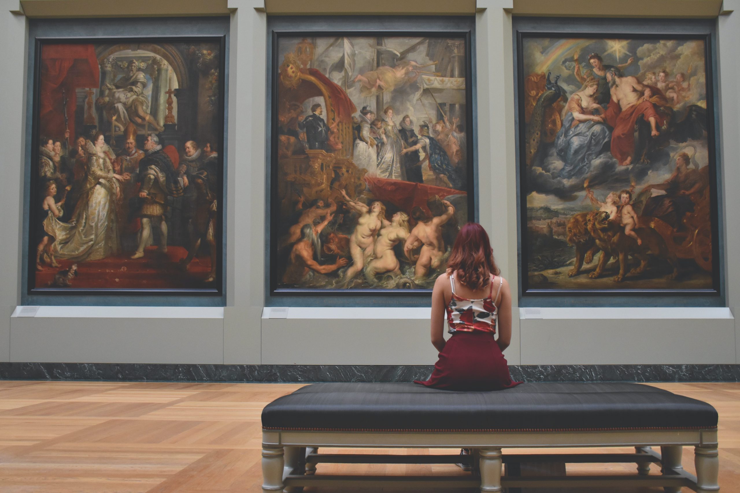 Vue arrière d'une jeune femme assise sur un ottoman regardant des tableaux artistiques